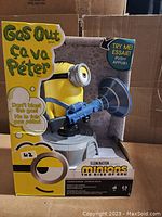 Front and side view of packaged Minions Gas Out game featuring yellow Minion figure holding blue cannon on gray base with bright yellow packaging.