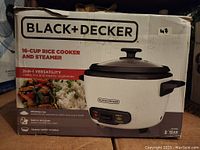 Box front showing Black & Decker branding, product image, and key features with 2-in-1 rice cooker and steamer functionality.