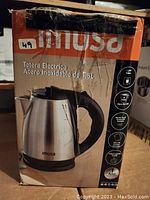 Box front showing imusa brand and product image of stainless steel electric kettle with black handle and lid, 1.8L capacity note in Spanish.