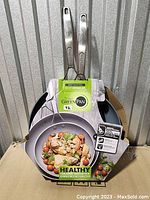 Two GreenPan ceramic nonstick frypans, 10 and 12 inches, with packaging visible showing 'Healthy Ceramic Nonstick' and some wear.