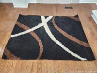 Rectangular black area rug with brown and cream wavy lines on hardwood floor