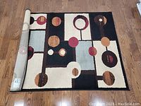 Photo showing the full geometric pattern on a beige and black rug, predominantly rectangular with circles and rectangles in various colors.