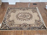 Full view of the beige and brown area carpet laid on wooden floor, showing overall condition and pattern.