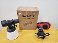 Lot contents showing spray gun with paint container, red power unit with cord, and original box on table.