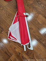 Folded red and white beach umbrella with white metal pole on wooden floor