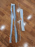 Five curtain rods laid out on hardwood floor, some partially wrapped in plastic with packaging torn.