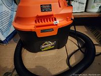 Orange and black Armor All utility wet/dry vacuum with flexible hose attached. Vacuum is compact, showing product label and model information on front.
