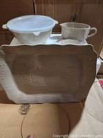 Photo showing four ceramic pieces: two mugs with handles, a medium dish, and a large platter with textured wood grain finish.