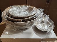 Stack of four white ceramic bowls of varying sizes and one ceramic spoon rest all wrapped in plastic
