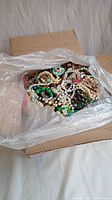 Opened USPS box with large quantity of assorted costume jewelry inside, visible are various beaded necklaces and bracelets.