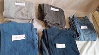 Five pairs of jeans laid flat: light gray, dark gray, blue, dark blue, and blue jean color. Each pair tagged with size 36x32 or similar.