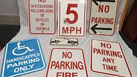 Seven vintage metal parking signs with various traffic and parking instructions arranged on a flat surface.