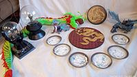 Overview of six dragon miniature plates, two plasma ball electric lights, two dragon figurines, green plush dragon, and two dragon plaques.