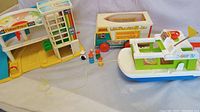 Photo showing Fisher-Price Little People garage, family camper, boat model 985, and five Little People figures arranged on a cloth surface.