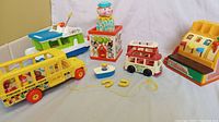 Clear front view of all vintage Fisher-Price toys including school bus, boat, van, Jack in the Box, and cash register.