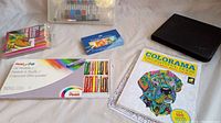 Full layout of art supplies including boxes of pastels, colored pencils, coloring book, and a black art case with brushes and erasers.