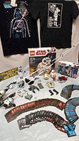 Overview of Star Wars collectibles including T-shirts, LEGO sets, fishing poles, miniature figures, and large collection of collectible cards spread out.