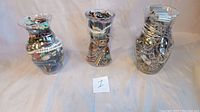 Three glass jars each densely packed with a variety of costume jewelry including beads, metal chains, rings, and bracelets.