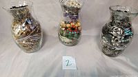 Three glass jars filled with a large assortment of vintage costume jewelry items seen from front
