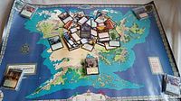 Magic The Gathering cards displayed on Middle Earth map poster, showing pile of various Magic cards with foil and artwork visible.