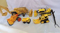 Five vintage construction toy vehicles arranged on white cloth, showing the Ford 755A tractor, Tonka trencher, hand roller, dump truck, and CAT plastic tractor.