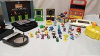 Overview photo showing most of the lot including the puzzle box, handheld electronics, mini characters, and other items
