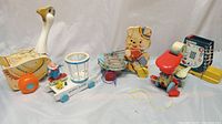 Photo of five vintage wooden Fisher Price toys including Mother Goose, Ziggy Zillo, Pelican pull toy, Wooden Shoe, and Humpty Dumpty, displayed together on a white cloth.