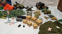 Wide view of vintage GI Joe and army green men toys with vehicles and accessories arranged on white background. Shows collection of action figures, toy tanks, army vehicles, plastic soldiers, and small jets.