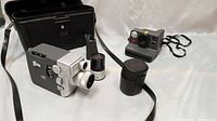 Photo of Canon vintage movie camera with attached zoom lens, extra zoom lens with case, Polaroid NOW instant camera, and black carrying case