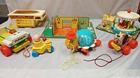Photo showing all seven vintage wooden toys and playsets in the lot arranged together including Playskool truck, toddler pull toy, turtle and puppy pull toys, play family house, camper, and Merry-Go-Round.