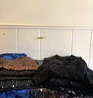 Top down view of folded sequin and lace tops in black, bronze, and blue colors.