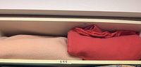 Two folded wool blankets, peach on left and red on right, shown together in a drawer or shelf.