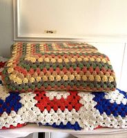 Two handmade crochet afghan blankets shown stacked. The top is a multi-color granny square pattern blanket with yellow, red, green, and gray yarn. The bottom blanket is large with red, white, and blue geometric crochet squares.