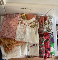 Photo of vintage aprons in assorted colors and patterns folded and stacked in a box