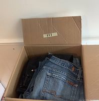 Box containing 7 pairs of 7 For All Mankind denim jeans in blue washes with visible back pockets and brand leather patches