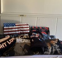 Photo of assorted folded graphic T-shirts showing various country and band-related prints including an American flag, OCR text, and artist images.