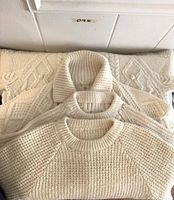 Three cream wool handknit sweaters stacked together showing detailed knit patterns and styles.