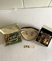 Jewelry lot displayed in three boxes: turquoise velvet box with multiple earrings and a bracelet; black velvet triangular box with silver-tone cuff links; white Pandora box with chain bracelet and earrings.