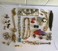 Top-down photo showing entire jewelry lot with necklace chains, earrings, rings, bracelets, pins including a fish-shaped pin.