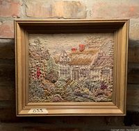 Full view of the framed crewel landscape embroidery showing the entire piece against a brick background.