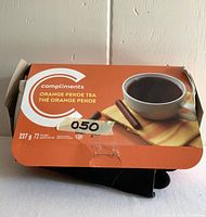 Closed orange tea box with black gloves underneath