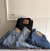 Six pairs of vintage Levi's 501 jeans folded and stacked, showing leather patches and red tabs on back pockets, with a mix of black and various blue denim washes.