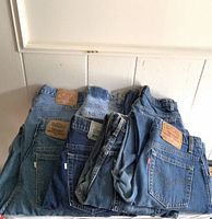 Stack of Levi's denim jeans in various blue washes with visible wear and Levi's leather patches on back waistbands.