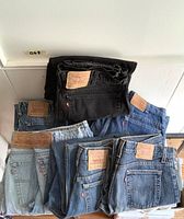 Eight folded pairs of jeans arranged in two rows on floor showing labels