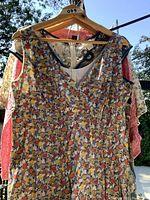 Front view of one sleeveless floral print dress on hanger against outdoors background