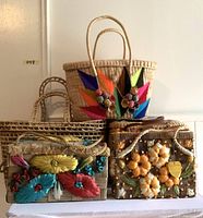 Front view of six woven handbags stacked on white surface, showing various colorful straw flower appliques and woven patterns.
