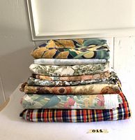 Front view of stacked vintage fabric pieces showing various patterns and colors including velveteen upholstery, florals, and plaid.