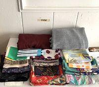 Overview of folded scarves on white surface, two solid knits on top, patterned silk scarves below