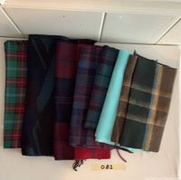 Eight vintage plaid scarves of various colors and lengths folded in a row showing patterns and fringes