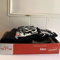Side view of folded T-shirts stacked in a box showing partial colorful graphics on black fabric